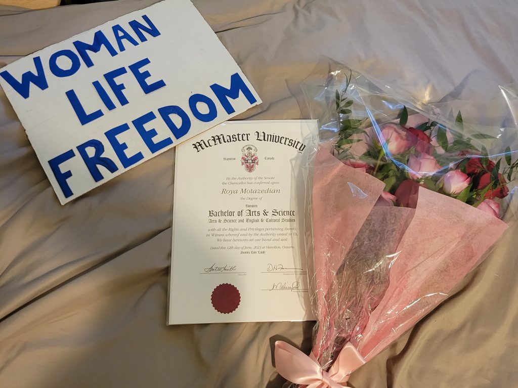 Image of a diploma, flowers, and a sign reading "Woman, Life, Freedom"