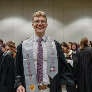 Graduate wearing "student athlete" sash smiling.